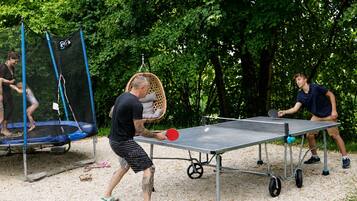 Ulkokäyttöön tarkoitettu pöytätennissetti, jossa on verkko ja joka on sijoitettu puiden ympäröimään paikkaan.