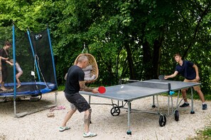 An outdoor table tennis setup with a net, surrounded by trees.