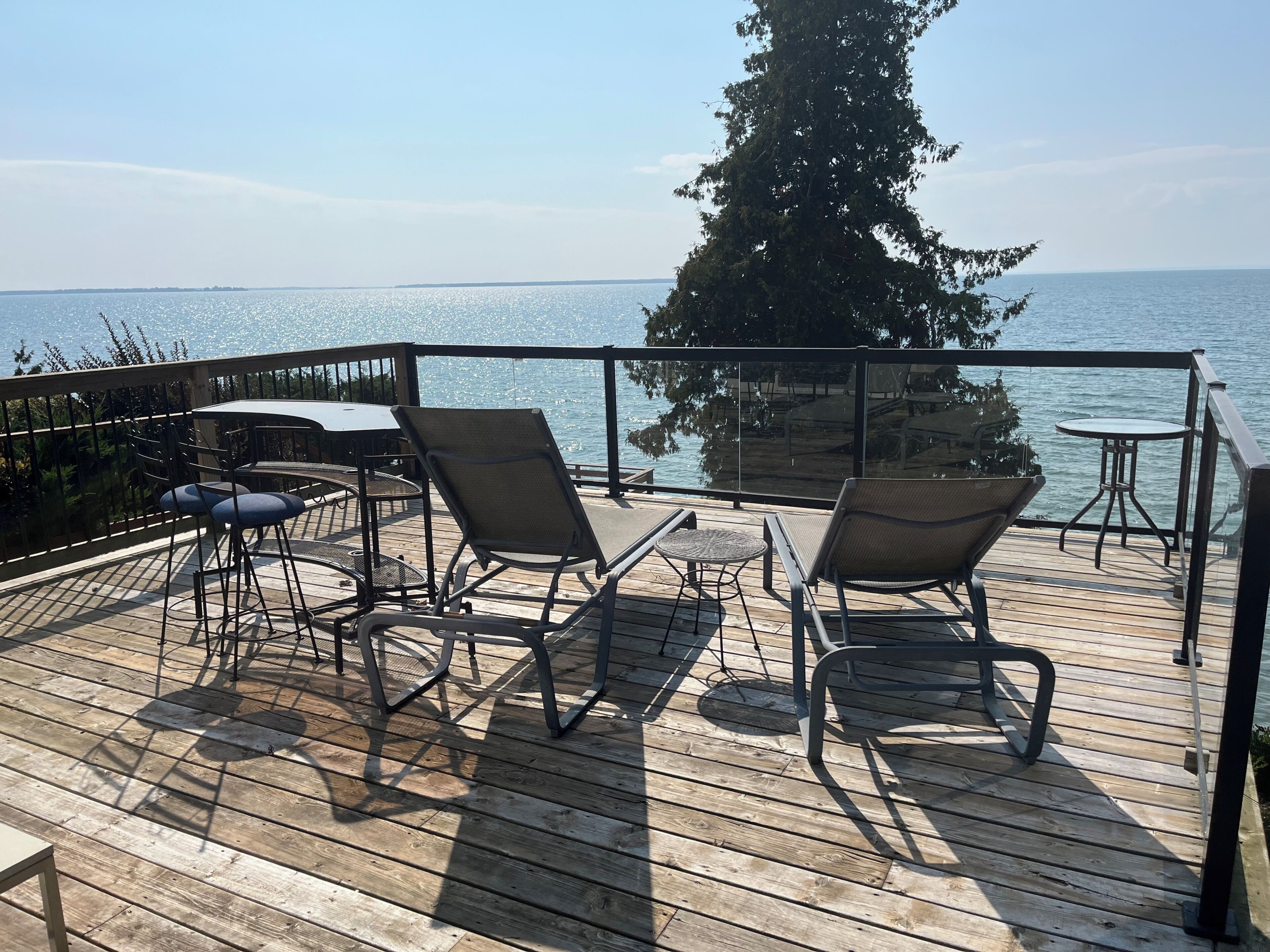 A wooden deck with outdoor furniture, including chairs and tables, overlooking a body of water.