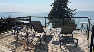 A wooden deck with outdoor furniture, including chairs and tables, overlooking a body of water.