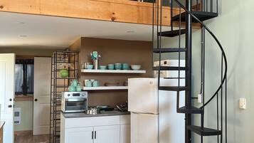 A kitchen with a wooden ceiling, a black spiral staircase, white cabinets, and a white refrigerator.