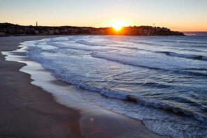 A beach with waves at sunset, a clear sky, and buildings in the background. - Rooftop-Pool Studio Stay in Bondi (Bondi)