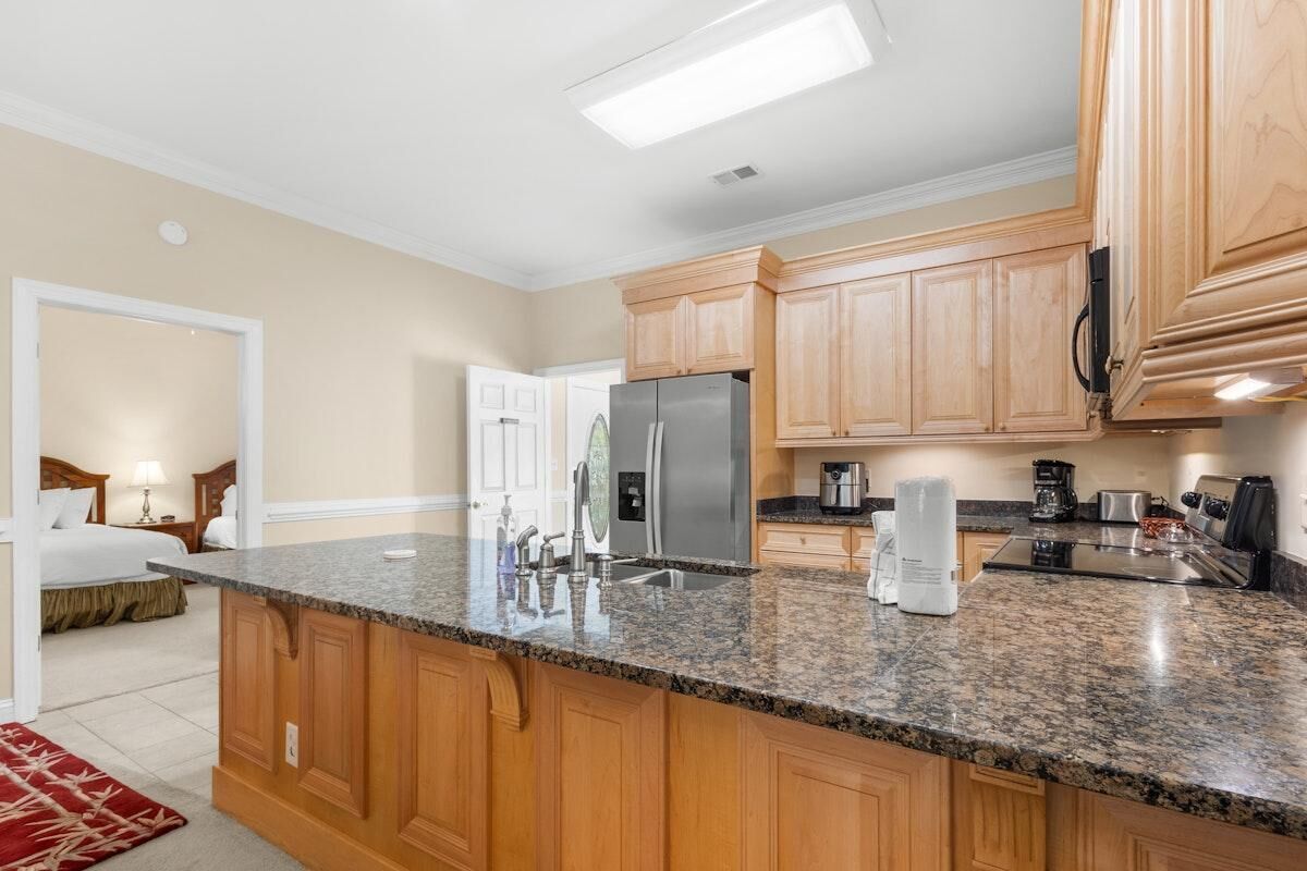 A kitchen with wooden cabinets, granite countertops, a refrigerator, and a coffee maker.