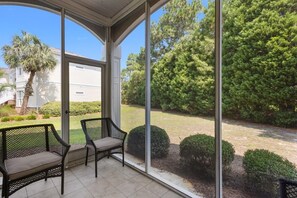 A covered patio with two chairs and a view of a well-maintained lawn and trees. - Tranquil Retreat in Prestigious Litchfield (Pawleys Island)