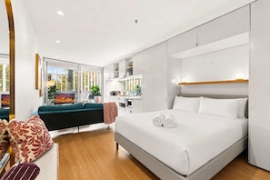 A modern hotel room with a large bed, a sofa, a dining area, and a view of the outdoors. - Poolside Studio Retreat Near Oxford Street (Darlinghurst)