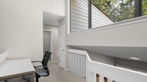 Ein Zimmer mit weißem Schreibtisch, schwarzem Bürostuhl und Blick ins Freie durch ein Fenster.