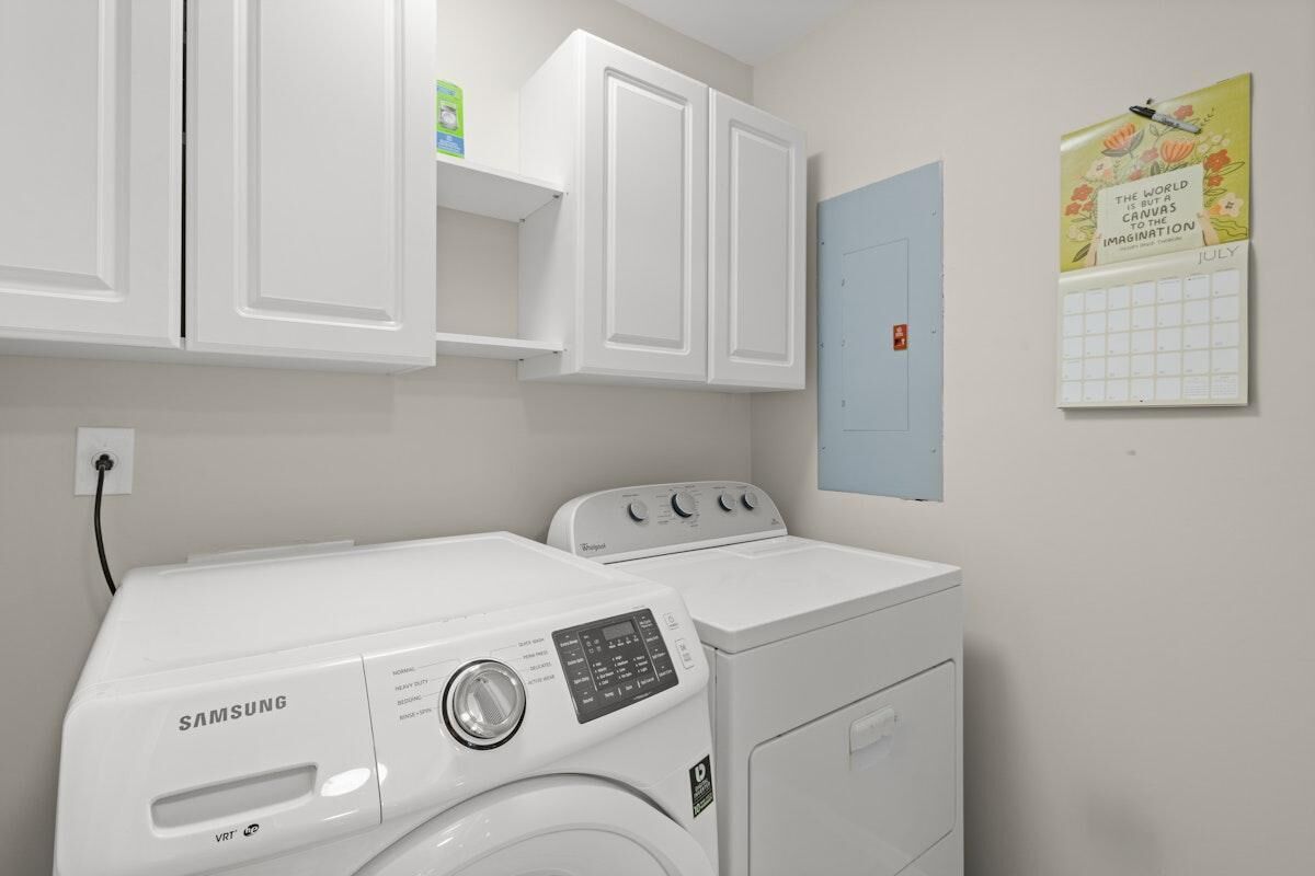 Une buanderie équipée d’un lave-linge et d’un sèche-linge Samsung, de placards blancs, d’un calendrier et d’une porte.