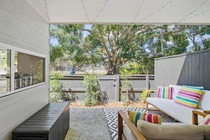 A patio with a white sofa, colorful pillows, a patterned rug, and a small tree.