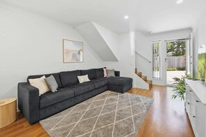 A modern living room with a sectional sofa, a geometric rug, and a staircase leading to an outdoor area.