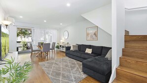 Una sala moderna con un sofá, una mesa de comedor con sillas, una escalera y vistas al exterior.