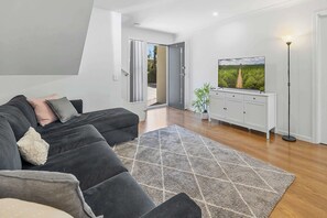Een moderne woonkamer met een hoekbank, een flatscreen televisie, een witte kast en een kamerkleed met dessin.