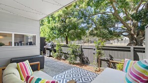 Un espacio de estar al aire libre techado con alfombra estampada, una parrilla de barbacoa y vistas a un patio trasero con árboles y una cerca.