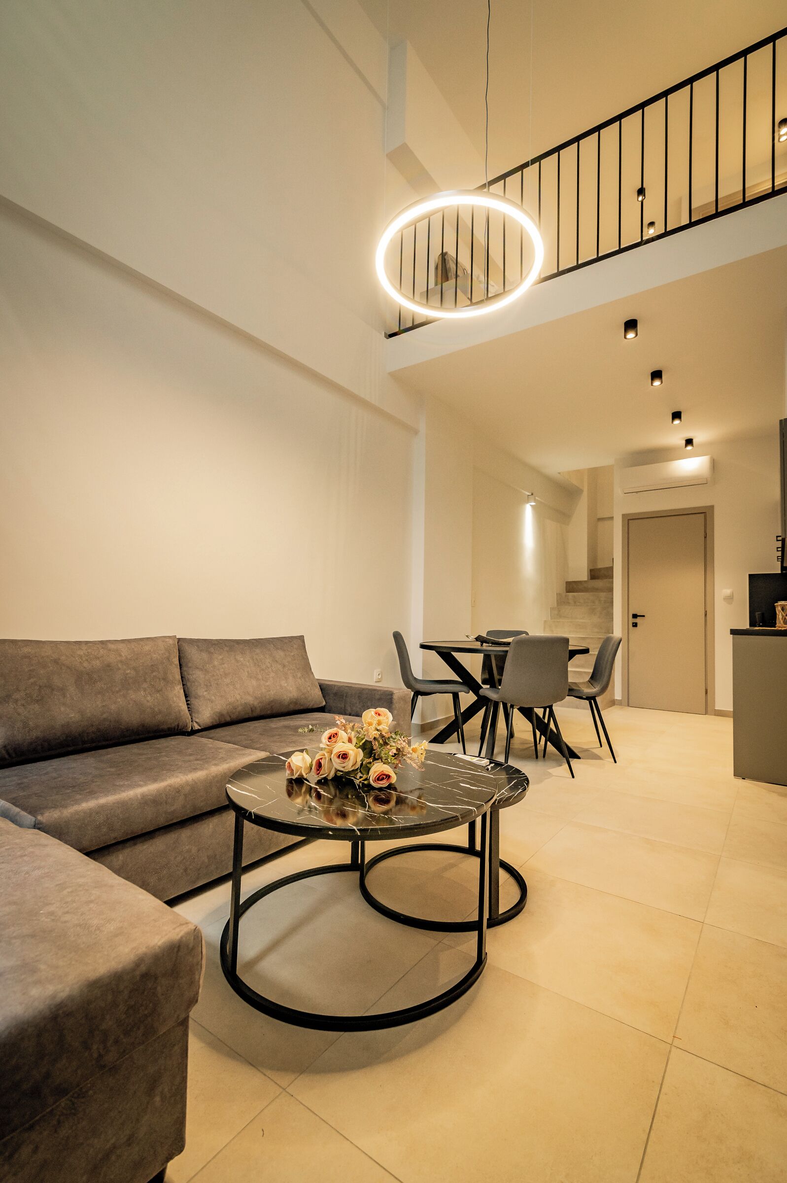 A modern living room with a sofa, a coffee table with flowers, and a dining area with chairs and a table.