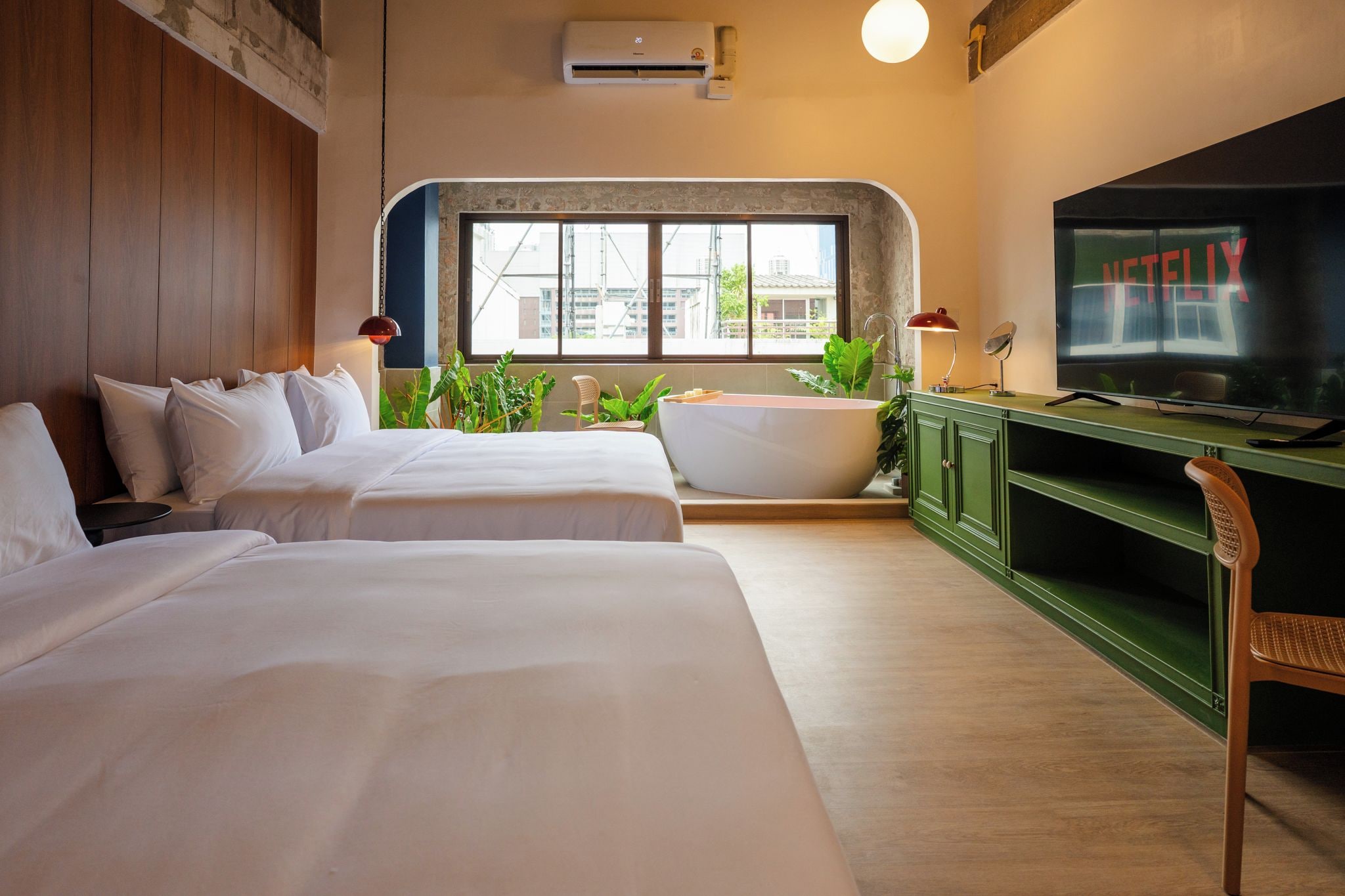 A hotel room with two beds, a bathtub, a TV, and a large window.