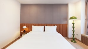 Una habitación de hotel con una cama, una mesita de noche, una lámpara y un espejo montado en la pared.