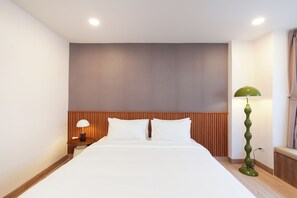 A hotel room with a bed, a nightstand, a lamp, and a wall-mounted mirror. - KAIM Ekkamai (Bangkok)