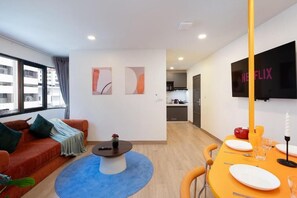 A modern living room with a sofa, a coffee table, a dining table set for two, and a TV mounted on the wall. - KAIM Ekkamai (Bangkok)