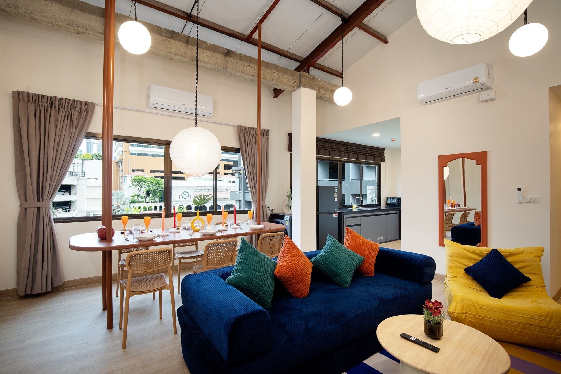 A modern living room with a blue sofa, yellow armchair, dining table set, and kitchen in the background.