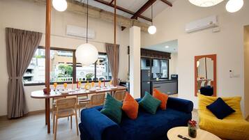 A modern living room with a blue sofa, yellow armchair, dining table set, and kitchen in the background.