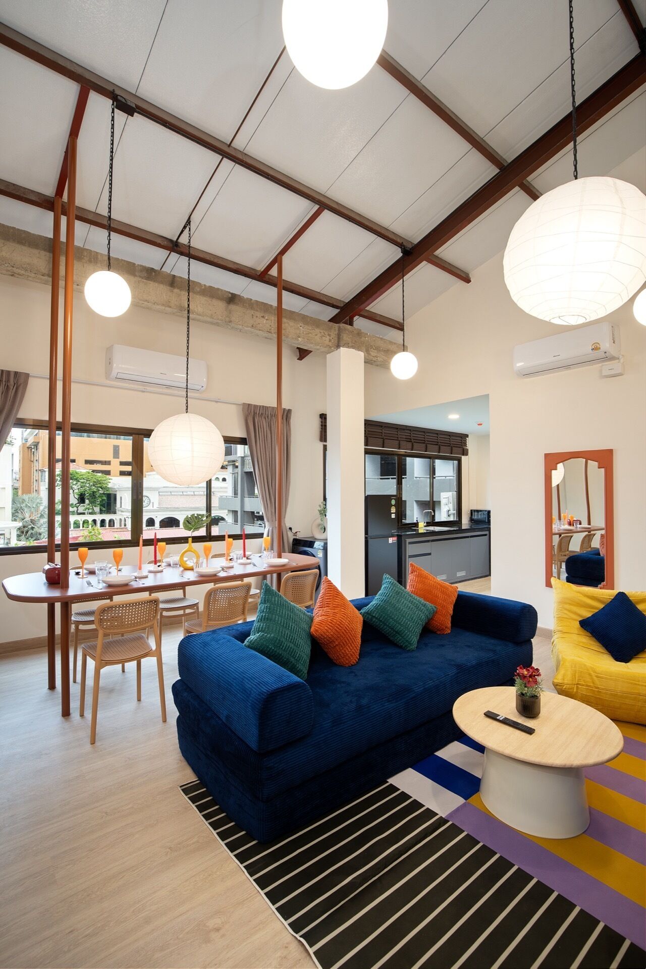 Ein modernes Wohnzimmer mit einem blauen Sofa, einem gelben Sessel und einem Essbereich mit Tisch und Stühlen.