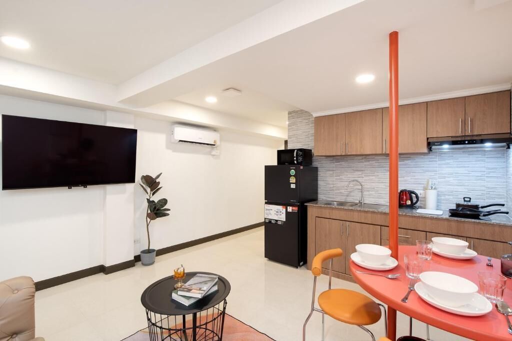 A modern kitchen with a flat-screen TV, a refrigerator, and a dining area with a table set for two.