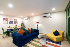 A living room with a blue sofa, a yellow armchair, a dining table with chairs, and a colorful striped rug. - KAIM Ekkamai (Bangkok)