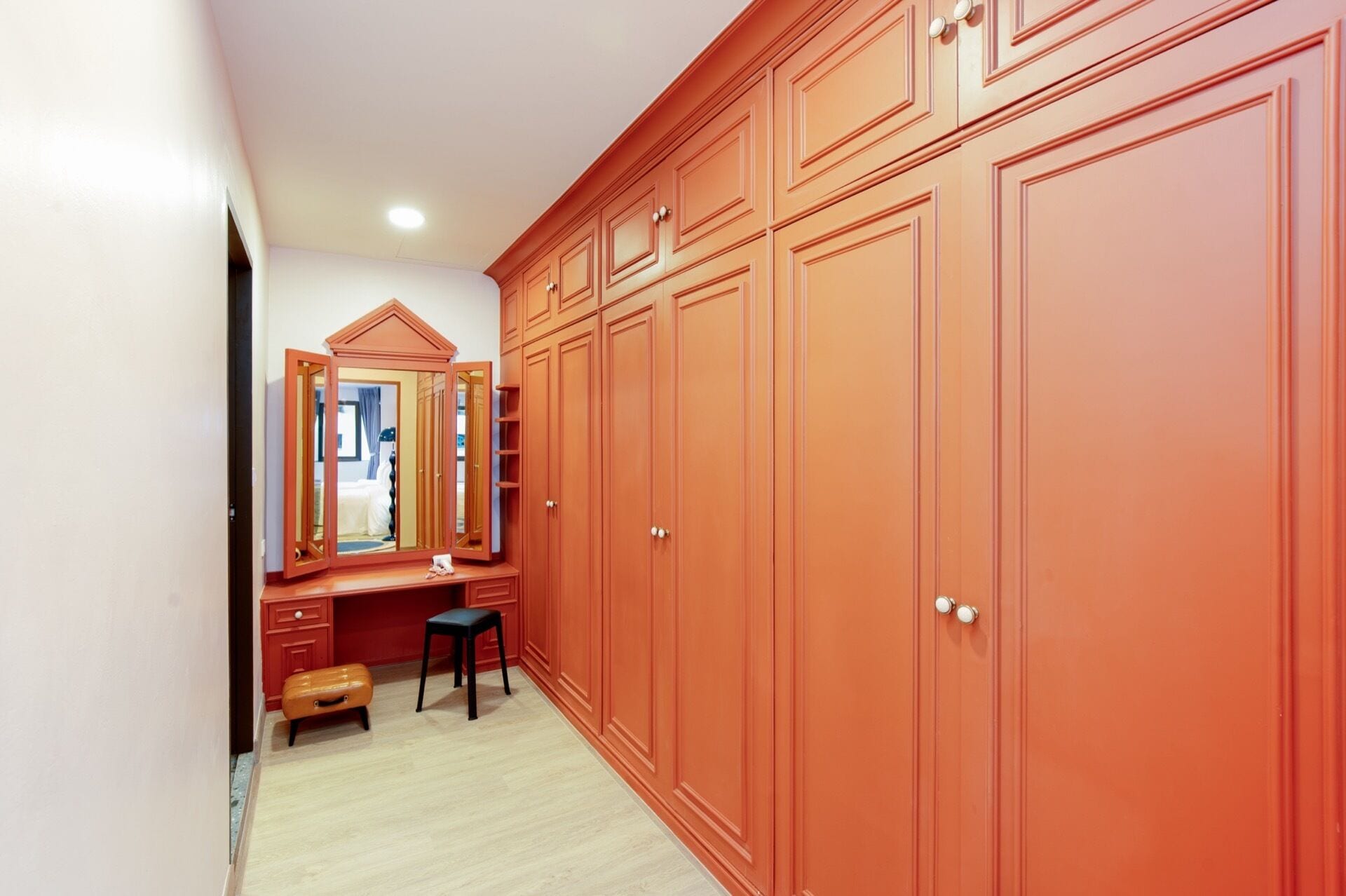 A walk-in closet with a large mirror, wooden cabinets, and a bench.