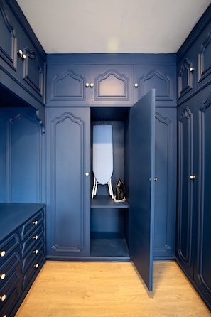 A room with a built-in wardrobe, a mirror, and a shelf with an ironing board and iron. - KAIM Ekkamai (Bangkok)