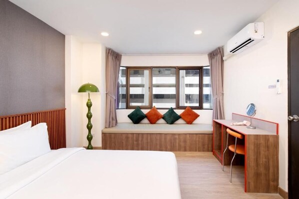 A hotel room with a bed, a desk, a window seat with cushions, and an air conditioning unit. - KAIM Ekkamai (Bangkok)