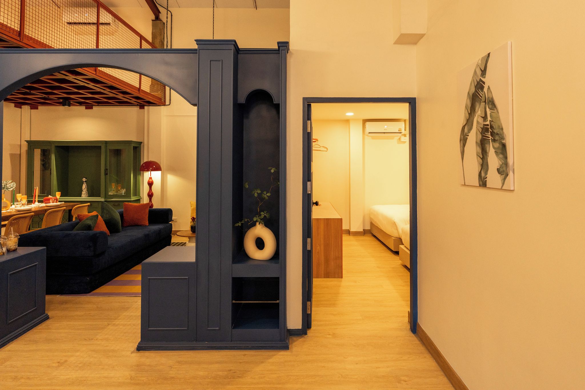 Ein modernes Interieur mit einem dunkelblauen Sofa, einem Essbereich mit einem grünen Schrank und einem Flur, der zu einem Schlafzimmer führt.