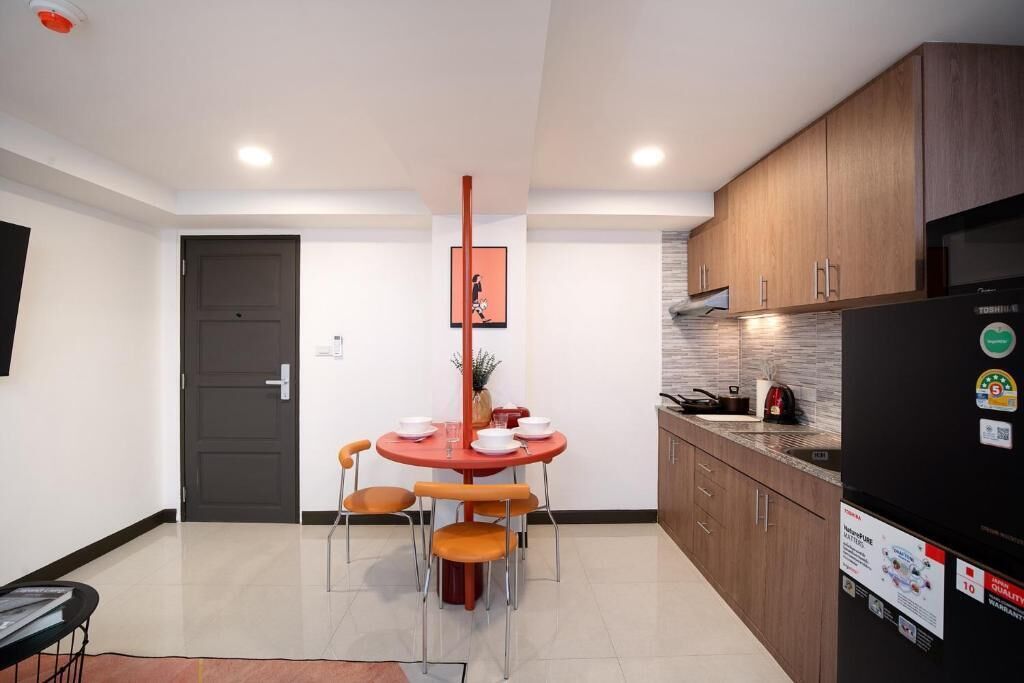 A modern kitchen with wooden cabinets, a black refrigerator, and a dining table with orange chairs.
