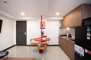 A modern kitchen with wooden cabinets, a black refrigerator, and a dining table with orange chairs. - KAIM Ekkamai (Bangkok)