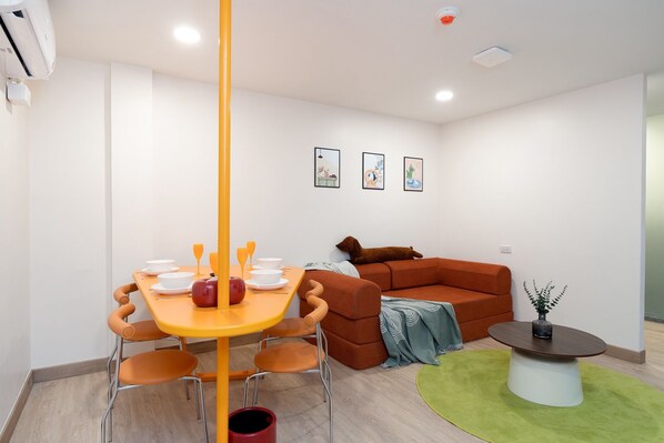 Un salon moderne avec une table à manger, des chaises orange, un canapé marron et une petite table basse.