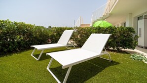 Two white lounge chairs on a well-maintained lawn with a green umbrella nearby, suggesting outdoor relaxation amenities. - Lovely 35 sqm apartment, for four people, located within the renowned Borgo 84 residential complex—which features two swimming pools, a sports area, and a cycle path. The property is just 3 km from the center of Marzamemi, one of Italy's most enchantin (Pachino)