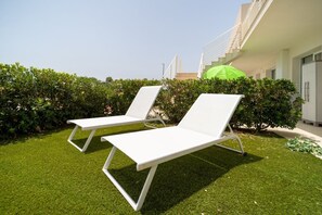 Zwei weiße Lounge-Stühle auf einer gepflegten Rasenfläche, in der Nähe ein grüner Sonnenschirm – deutet auf Entspannung im Freien hin.