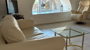 A living room with a sofa, armchair, and a glass coffee table. A television is on a small table to the left.