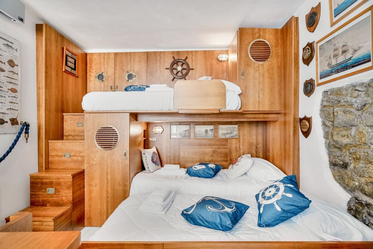 Ett rum med en våningssäng, träpanel på väggarna, en dekorativ skeppsrat och en inramad fiskkarta.
