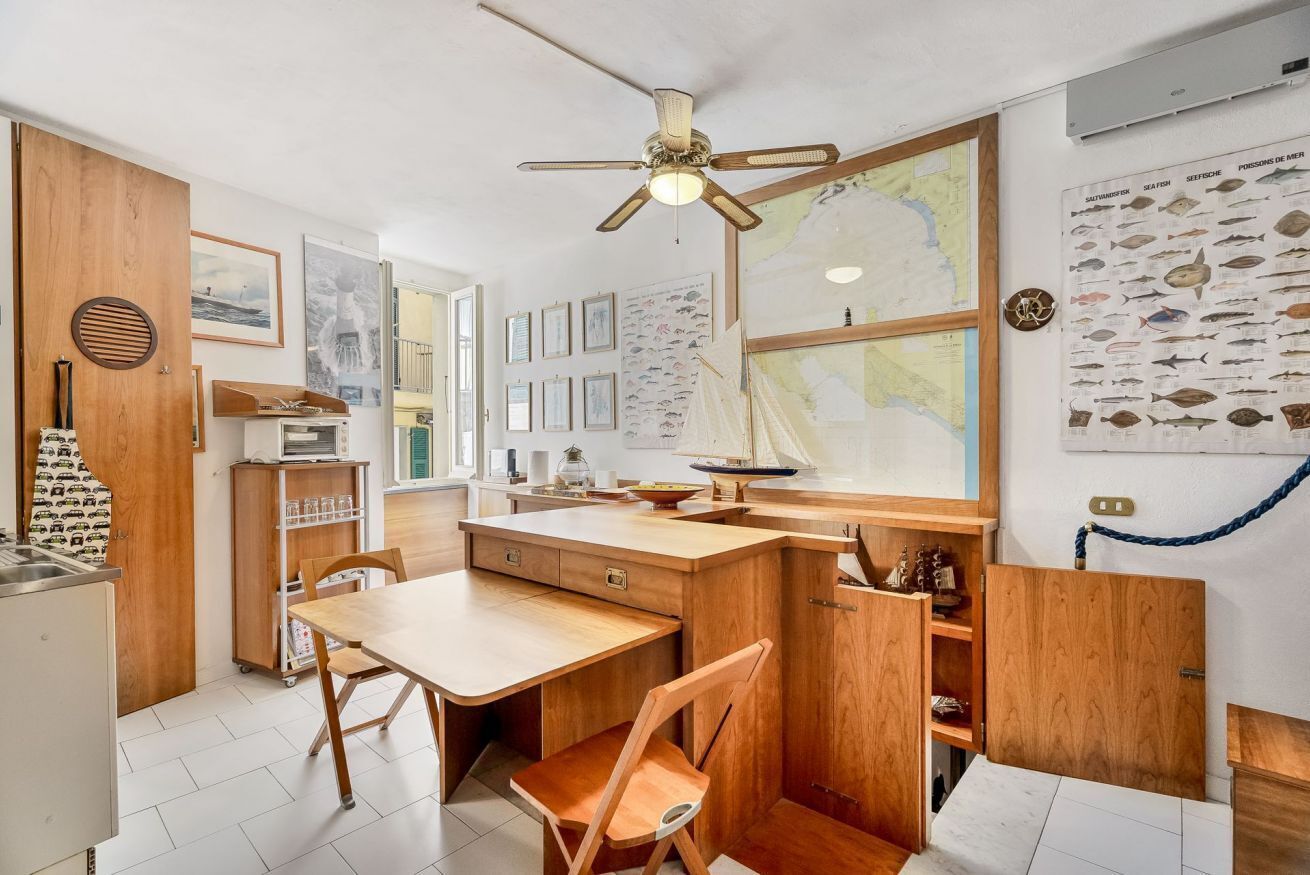 Cocina compacta con muebles de madera, una mesa de comedor y sillas. Hay un ventilador de techo, un mapa en la pared y decoración temática náutica.