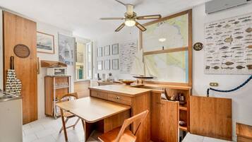 Cocina compacta con muebles de madera, una mesa de comedor y sillas. Hay un ventilador de techo, un mapa en la pared y decoración temática náutica.