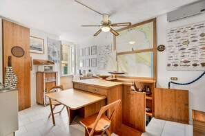 Eine kompakte Küche mit Holdekor, einem Esstisch und Stühlen. Ein Deckenventilator, eine Karte an der Wand und eine maritime Dekoration sind ebenfalls vorhanden.