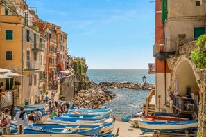 A coastal town with boats docked along the shore, buildings with balconies, and a clear view of the sea. - [LaCasaDelCapitano]Riomaggiore-Near the station (Riomaggiore)