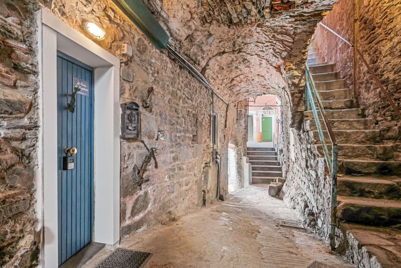 En smal stengång med en blå dörr, en trappa och en utsikt mot en grön dörr i slutet.