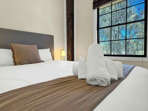 Ein Hotelzimmer mit einem großen Bett, einem Kopfteil, einem Fenster mit Blick auf Bäume und einer Lampe auf dem Nachttisch.