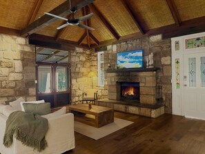 Ein Wohnzimmer mit Steinböden, einem Kamin, einem Deckenventilator und einem darüber montierten Fernseher.