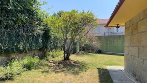 A backyard with a small tree, a grassy area, a stone wall, and a building with a tiled roof.