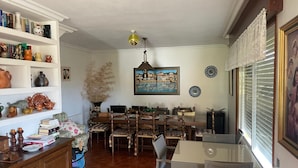 A dining area with a wooden table and chairs, a bookshelf with various items, and a painting on the wall.