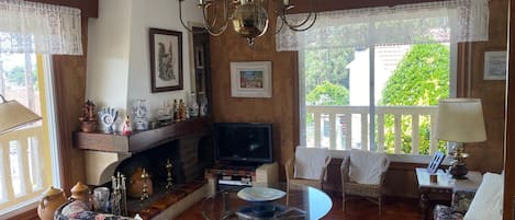 Una sala de estar con chimenea, televisión y balcón con vistas a zonas verdes.