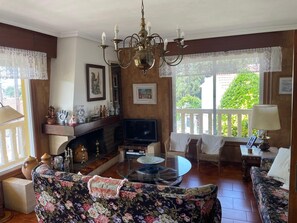 Uma sala de estar com lareira, televisão e varanda com vista para o verde.
