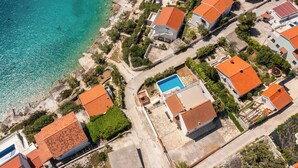 Ett flygbildsbild av ett bostadsområde vid kusten med hus, en swimmingpool och en fri utsikt över havet.