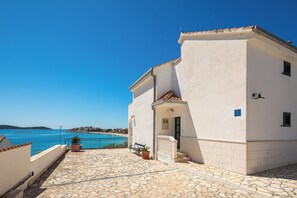 Ein Küstengebäude mit Kiesweg, einem kleinen Balkon und freiem Blick auf das Meer.